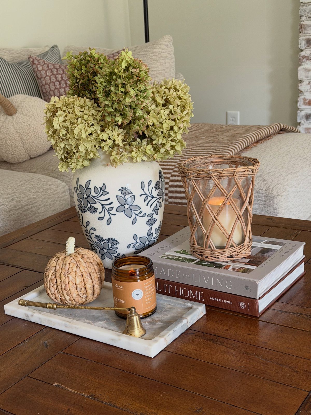 Floral vase, small pumpkin, and candles arranged on a wooden coffee table.