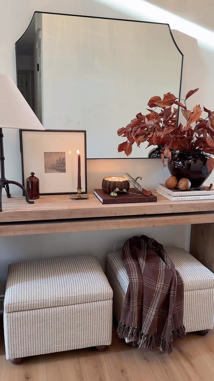 Autumnal entryway decor featuring a wooden console table with dried leaves, candles, and a large mirror.