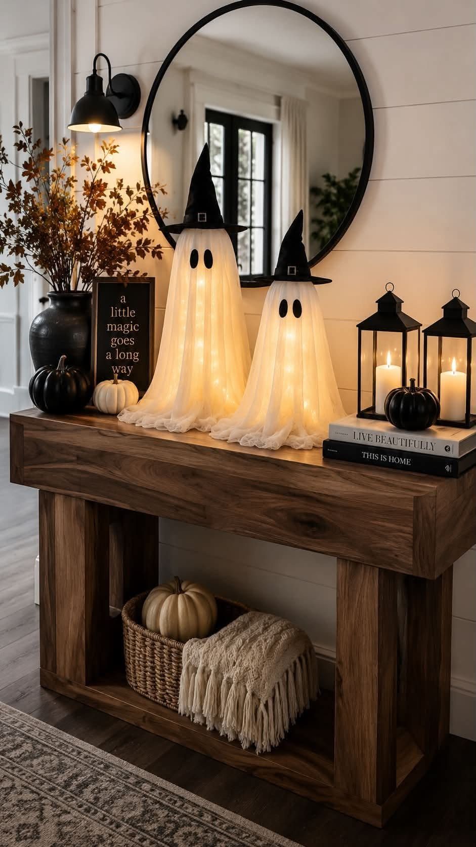 Ghost-shaped candle holders and black lanterns decorating a wooden entryway console table.