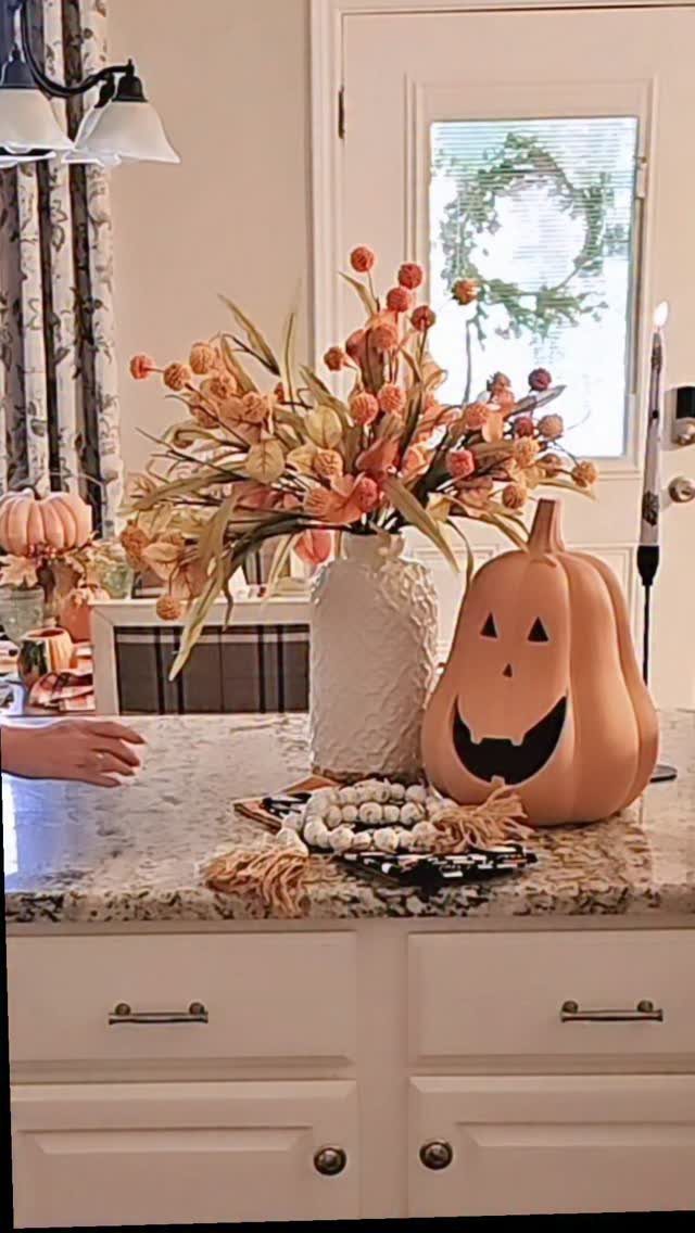 Peach Jack O'Lantern pumpkin and orange flowers on a granite kitchen countertop.