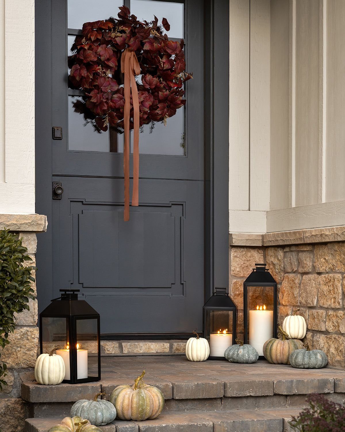 Black metal lanterns with glowing candles sit on stone steps surrounded by small decorative pumpkins.
