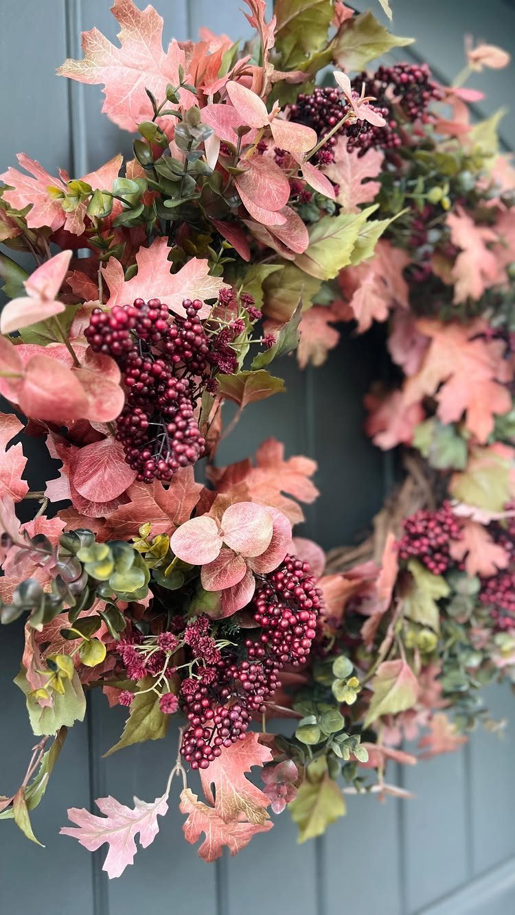 An autumn wreath featuring peach leaves and dark red berries hanging on a grey door.