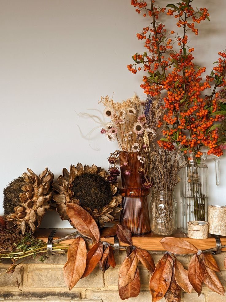 Dried sunflowers and orange berry branches arranged in vases on a wooden mantelpiece.