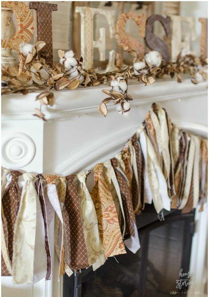 Fabric banner with patterned strips hanging across a white fireplace mantel decorated with cotton bolls.