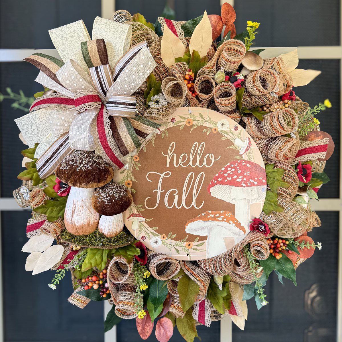 A decorative fall wreath with burlap, mushrooms, and a central sign saying hello Fall.