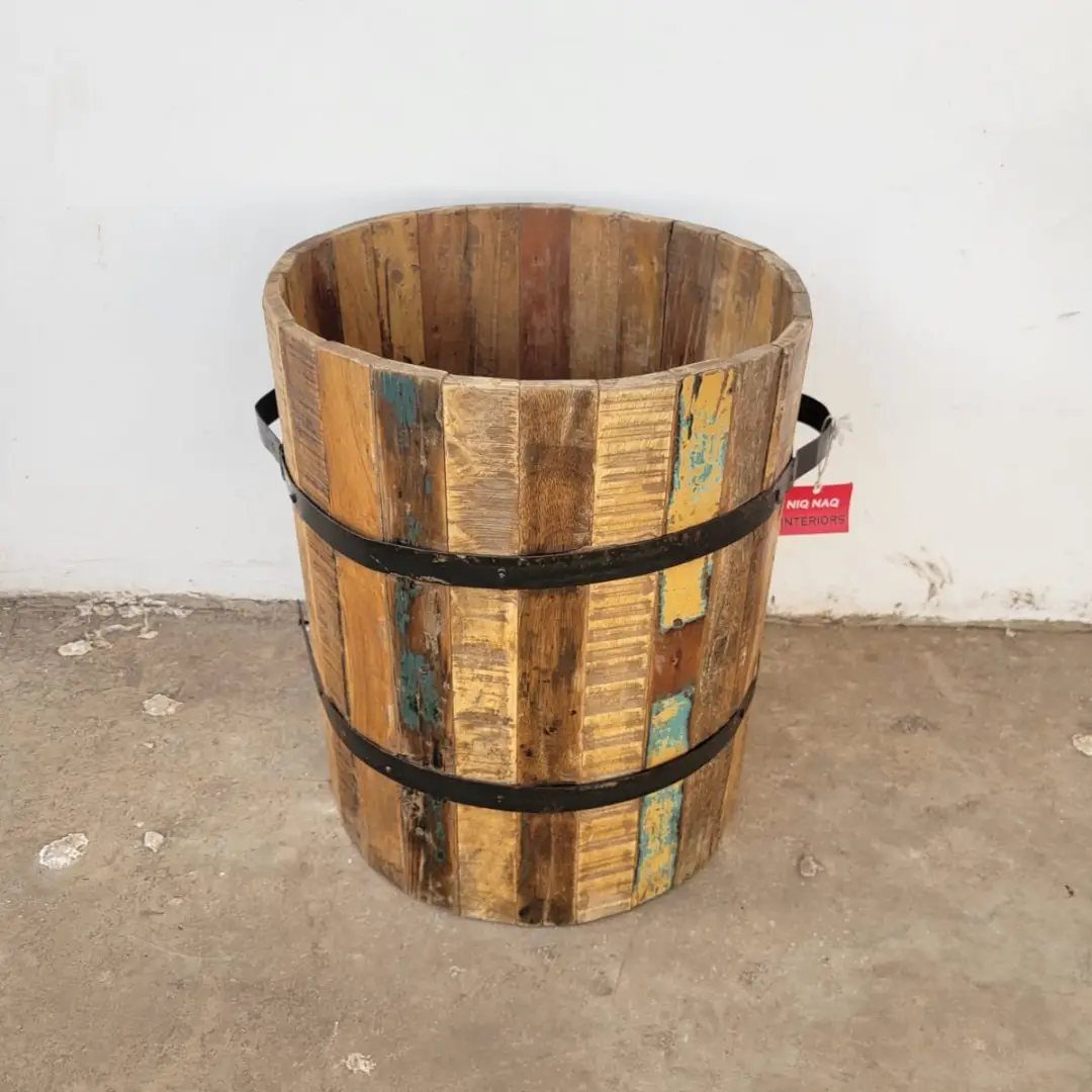 A rustic wooden bucket with black metal bands sitting on a concrete floor.