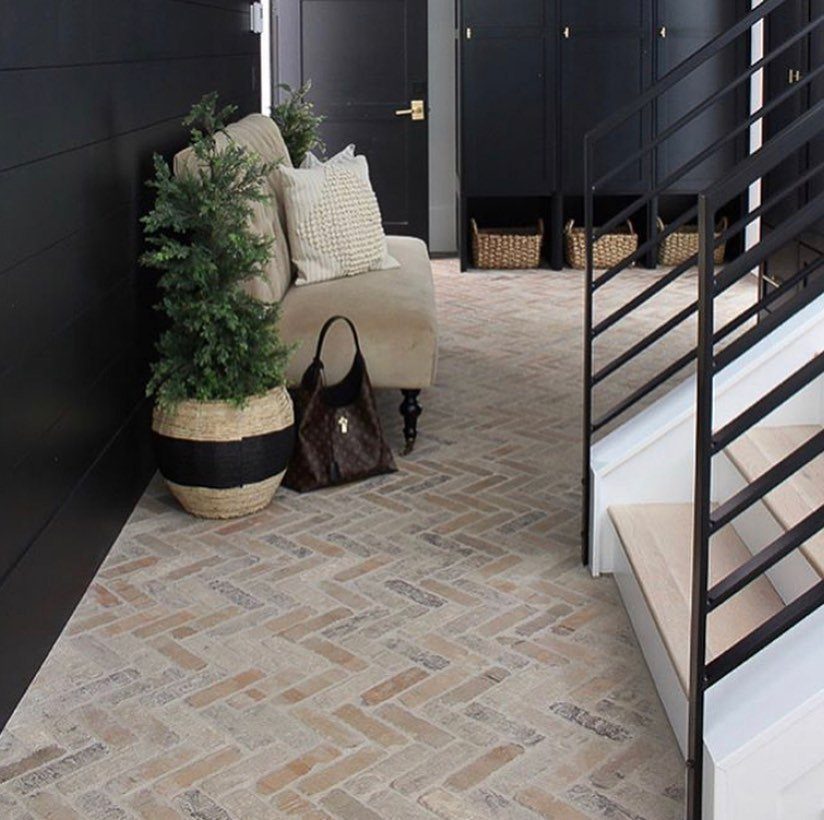 Large green plant in a woven basket beside a beige armchair on herringbone tile.