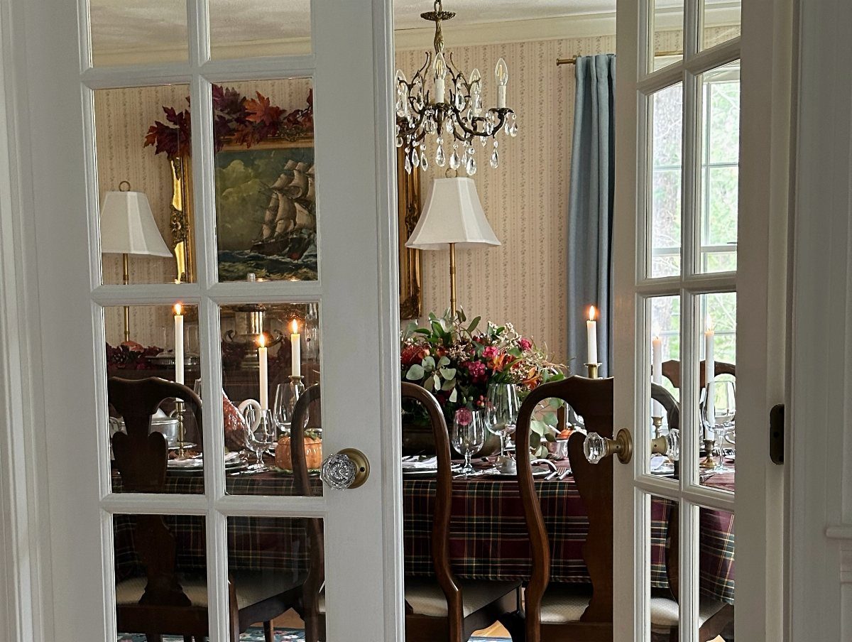 A dining room with a chandelier, lamps, and lit candles seen through French doors.