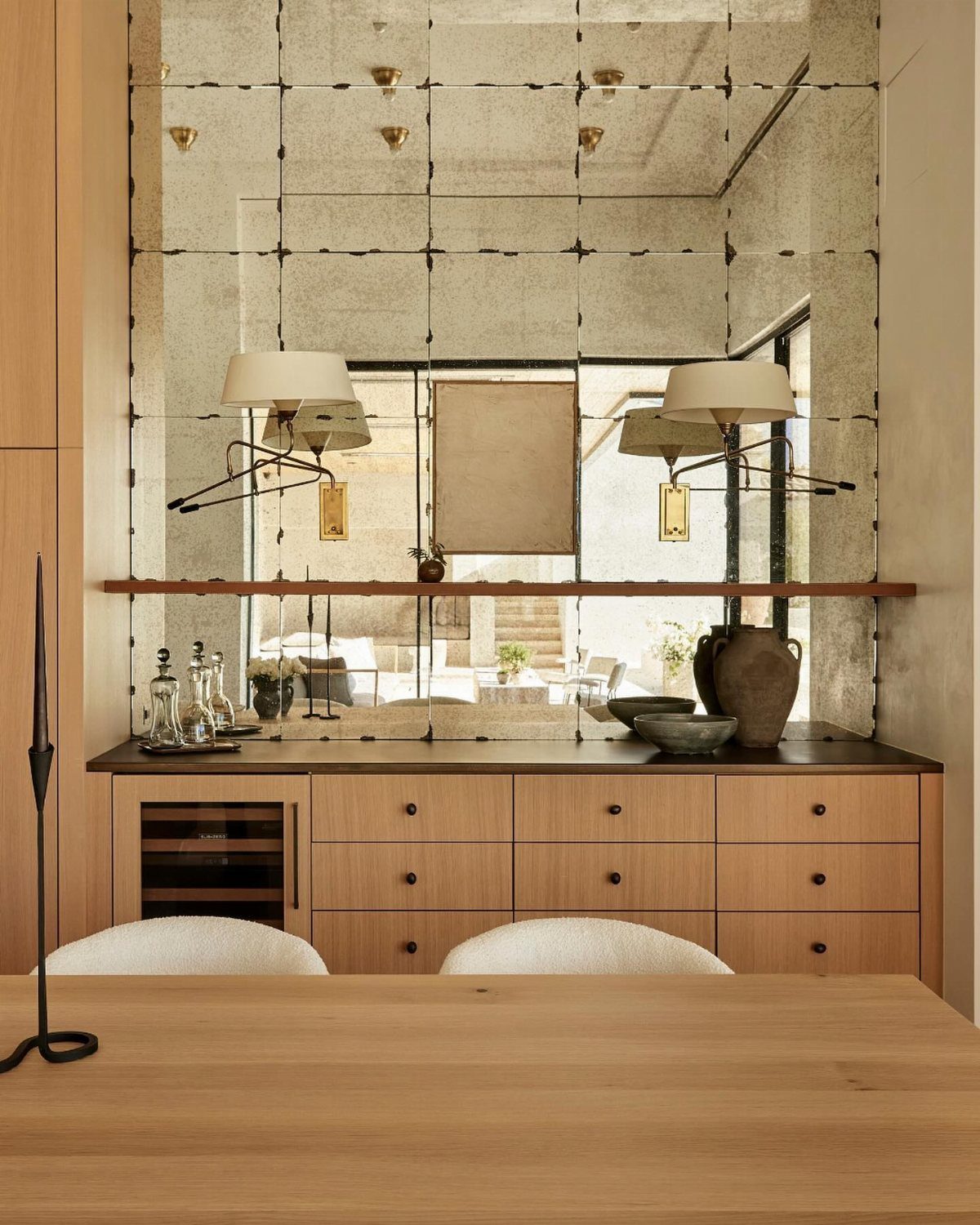 Large antiqued grid mirror mounted above a light wood sideboard in a bright room.