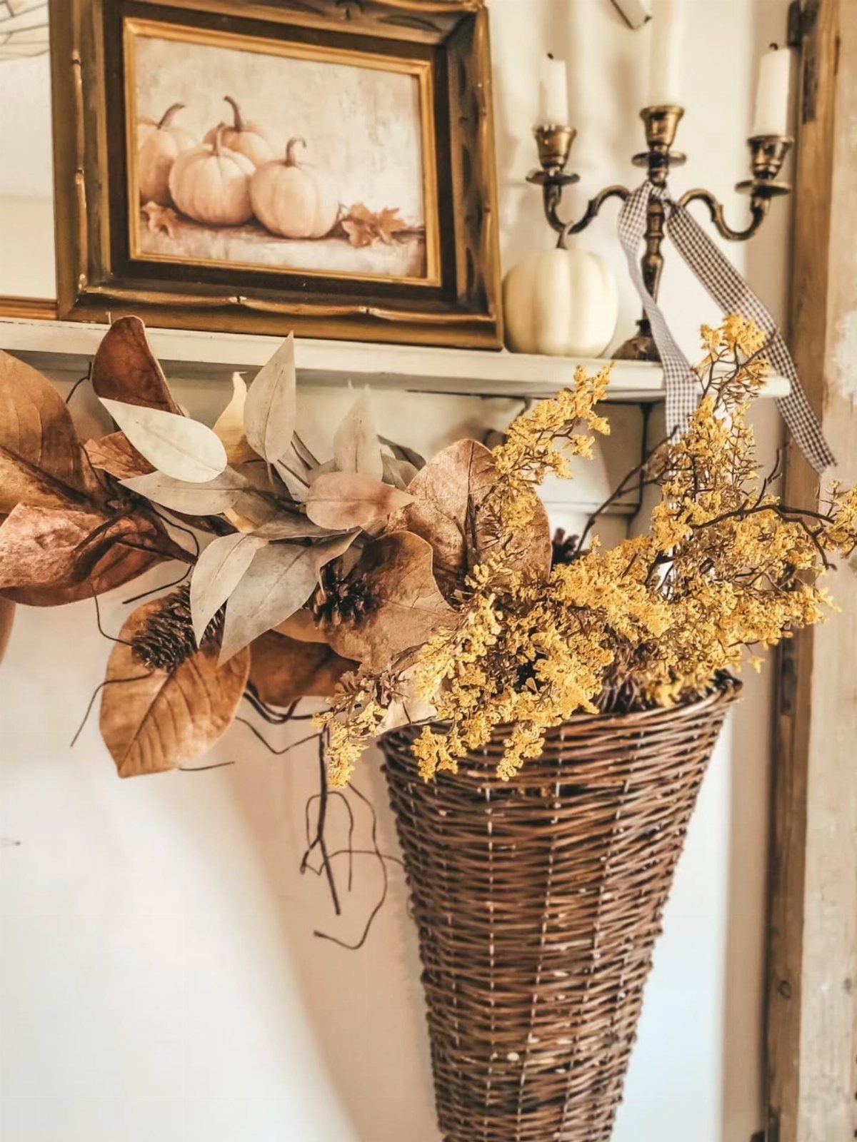 Wicker basket with dried yellow flowers and large brown leaves on a white shelf.