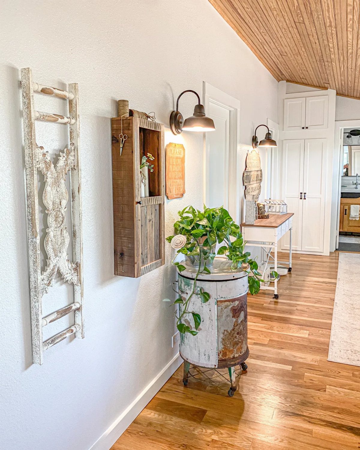 Rustic hallway with a reclaimed wood wall cabinet, white ladder, and metal plant stand.