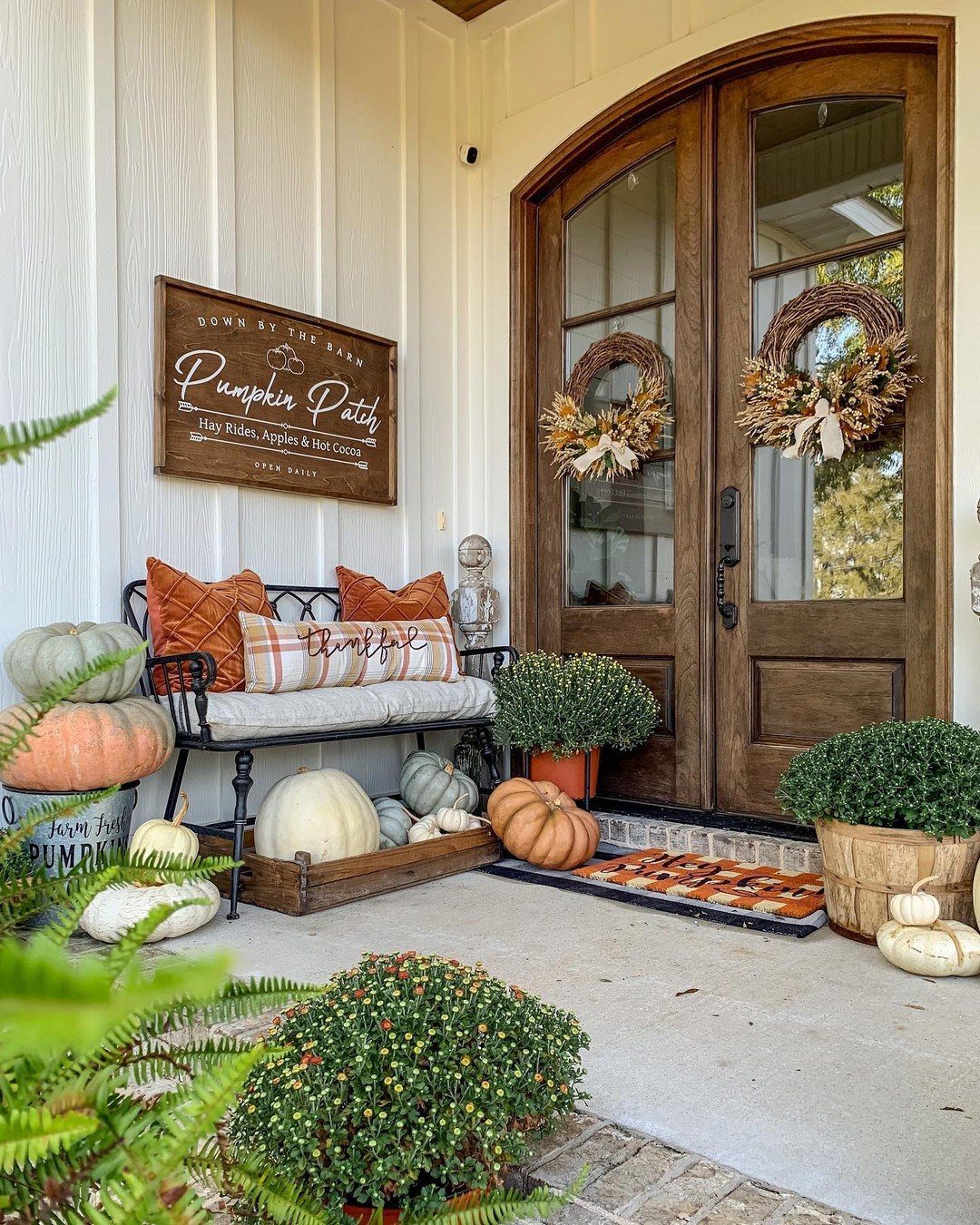Two grapevine wreaths hanging on arched wooden double doors surrounded by autumn pumpkins.