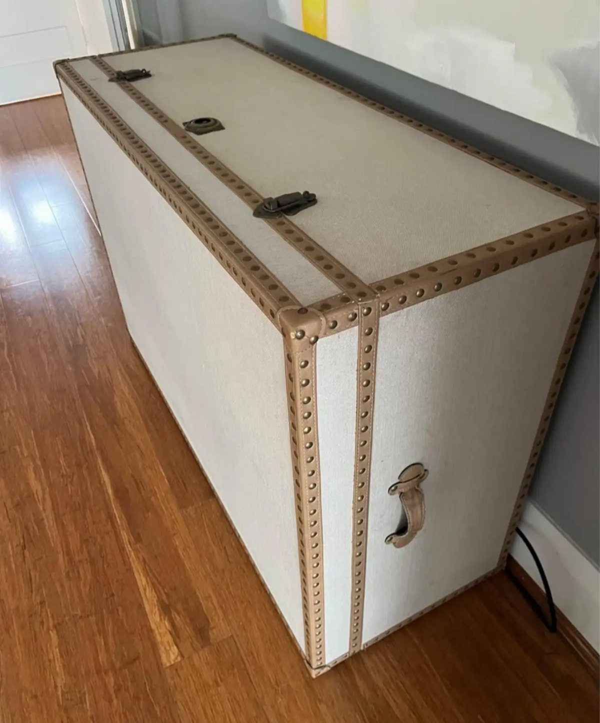 A large cream and tan studded storage trunk sitting on a hardwood floor.