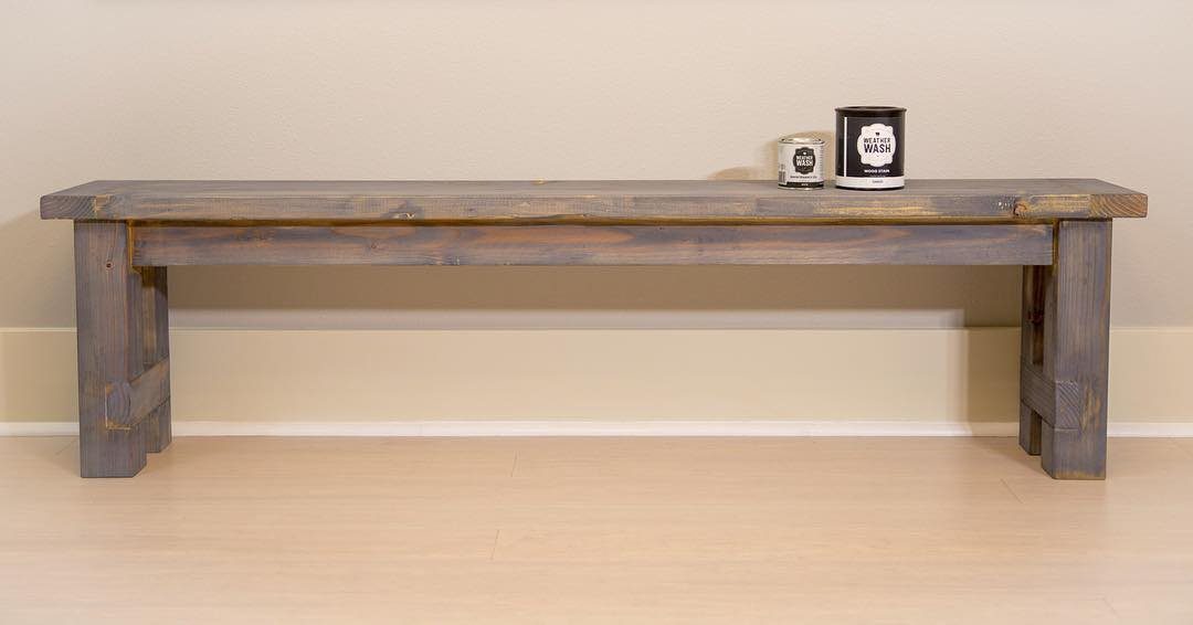 A long rustic wooden bench with a weathered grey finish against a beige wall.
