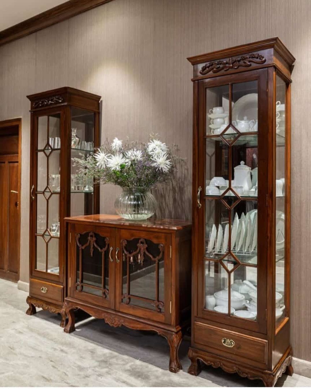 Three dark wood antique cabinets and a sideboard with white flowers in a vase.