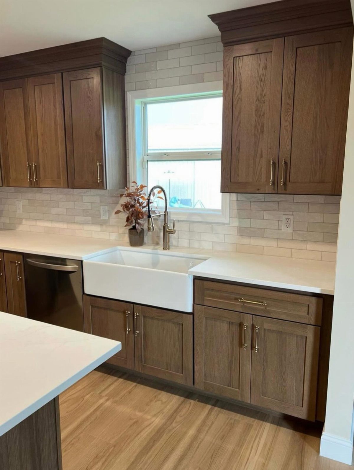 White apron front farmhouse sink installed in a kitchen with wood cabinets and subway tile backsplash.