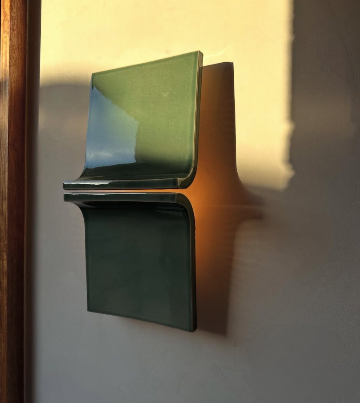 A sage green ceramic wall sconce with a folded geometric design on a wall.