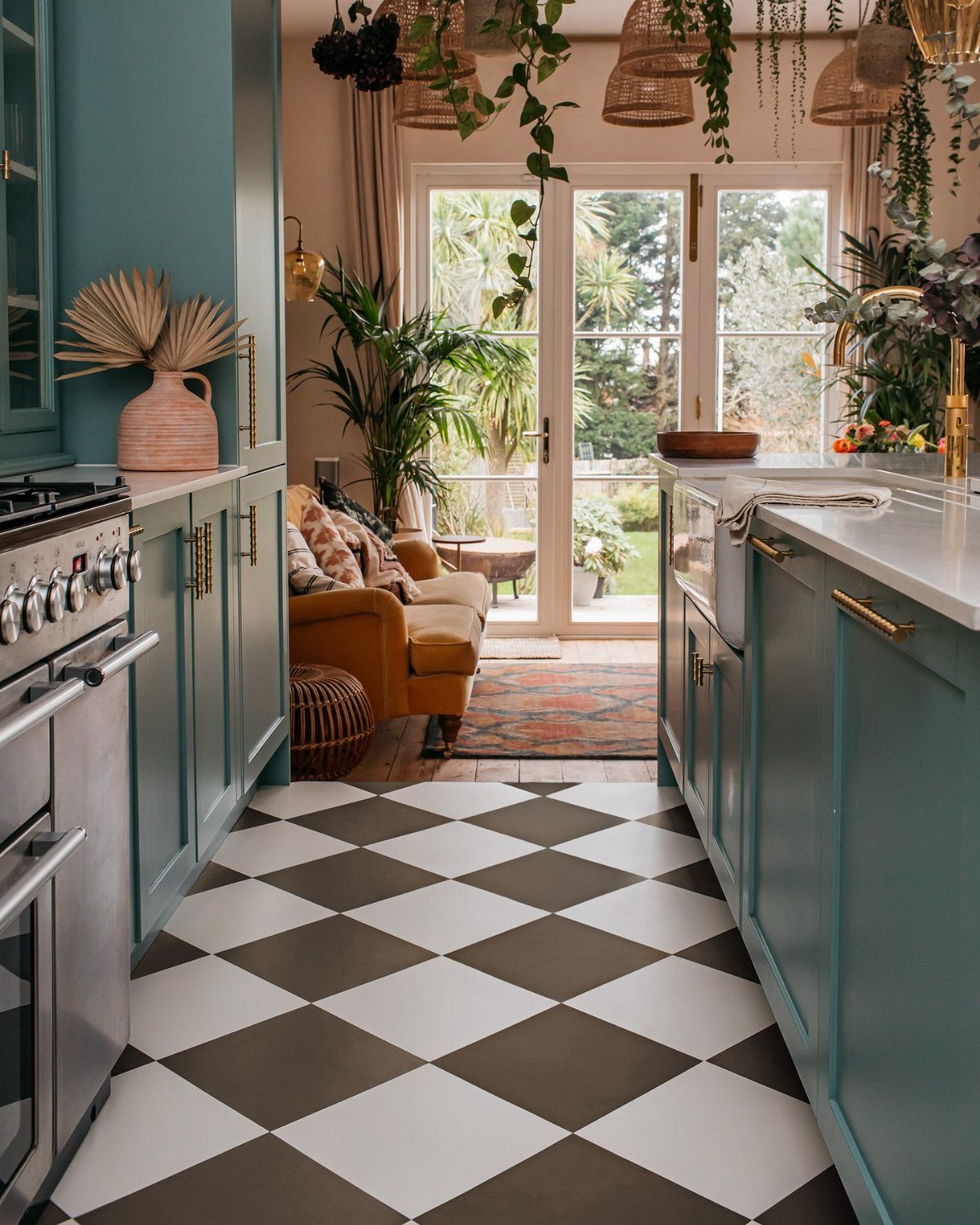 Black and white checkerboard tile flooring in a teal kitchen leading to a sunlit living area.