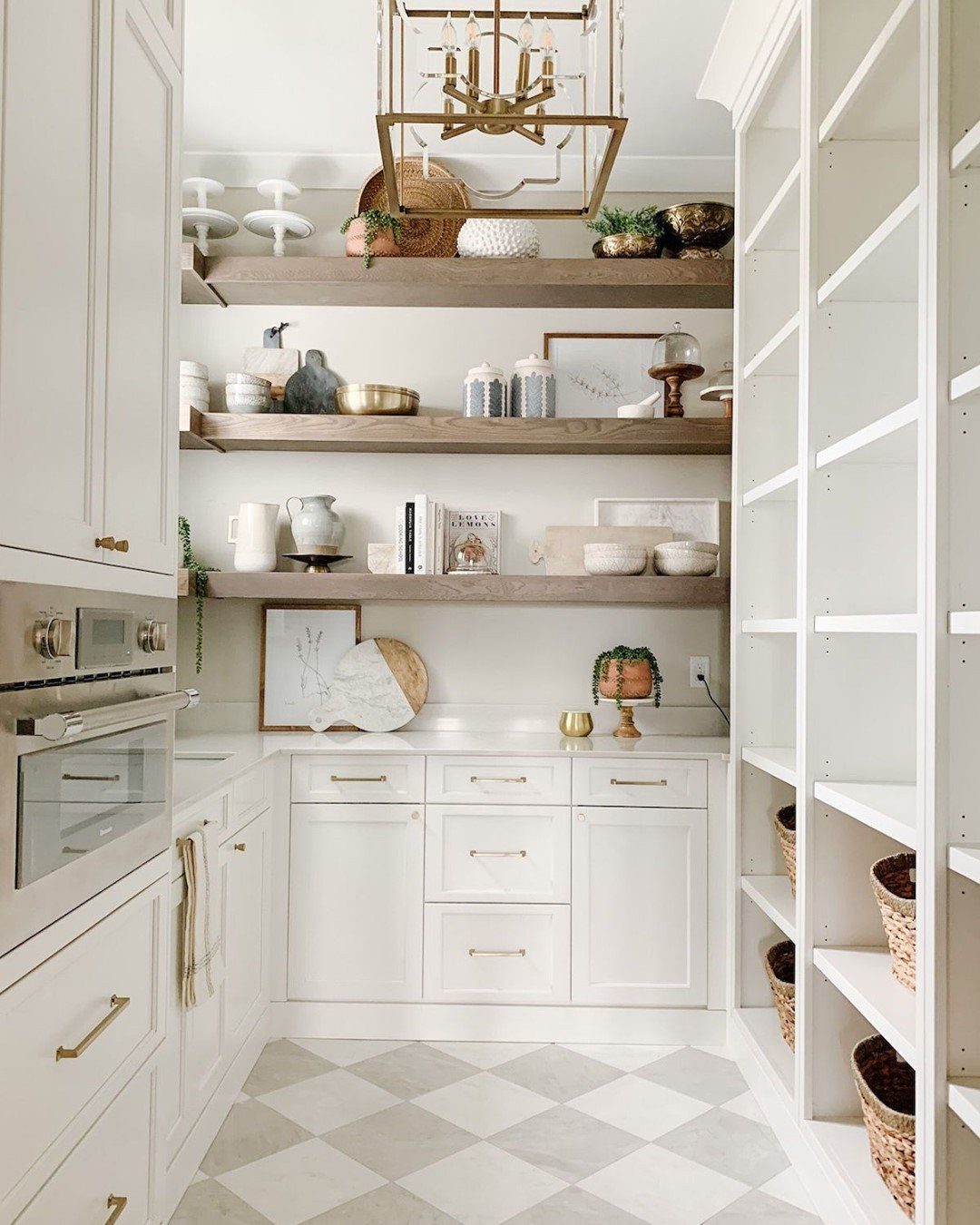 White farmhouse kitchen with wooden open shelves, white cabinetry, and a grey and white checkerboard tile floor.