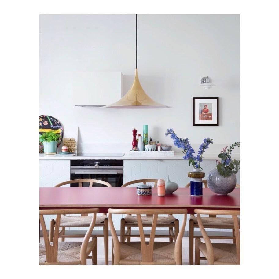 A red dining table with wooden chairs sits in a bright kitchen with colorful decor.