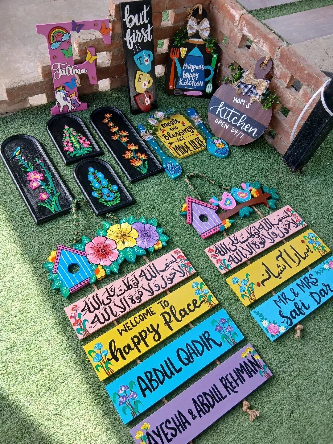 Hand-painted colorful wooden signs with floral patterns and text laid out on green grass.