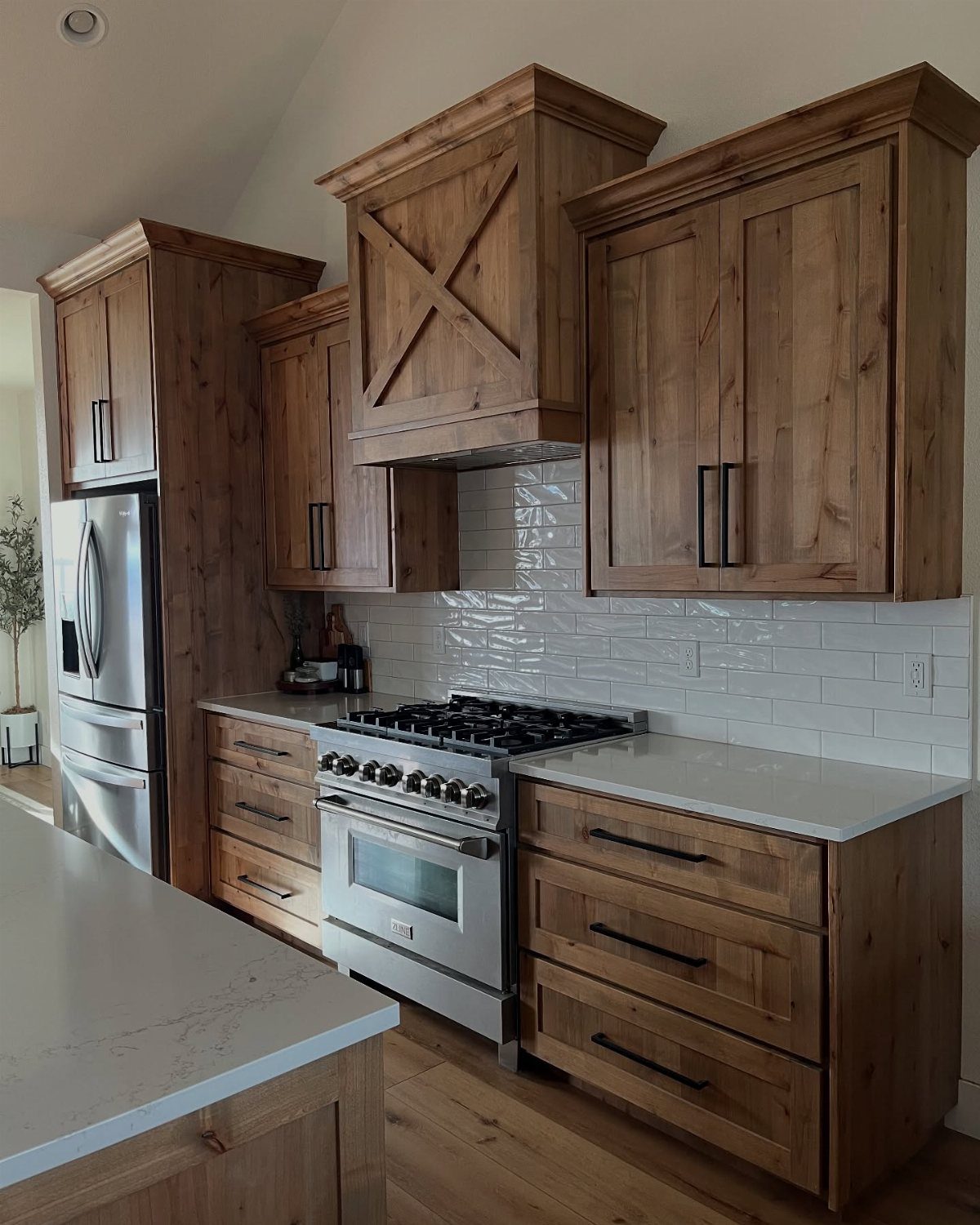 Wooden kitchen cabinets with black hardware, white subway tile backsplash, and stainless steel appliances.