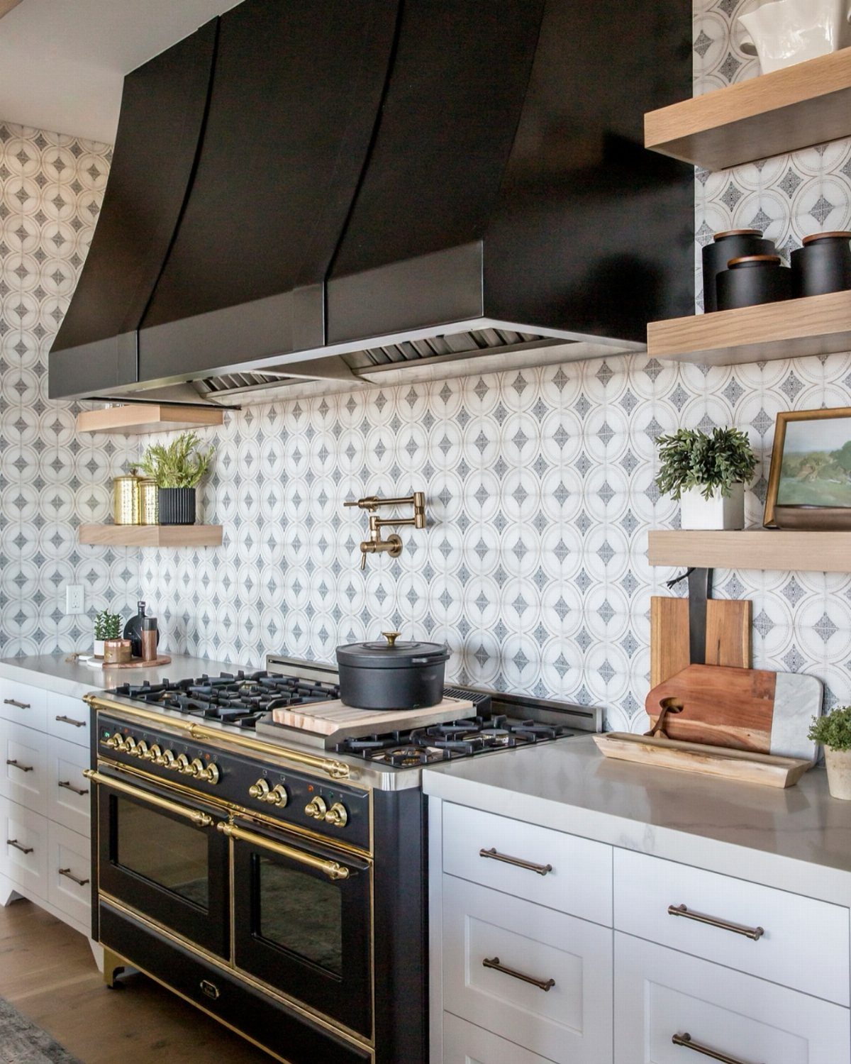 A modern kitchen with a patterned backsplash, black range hood, and professional stove.