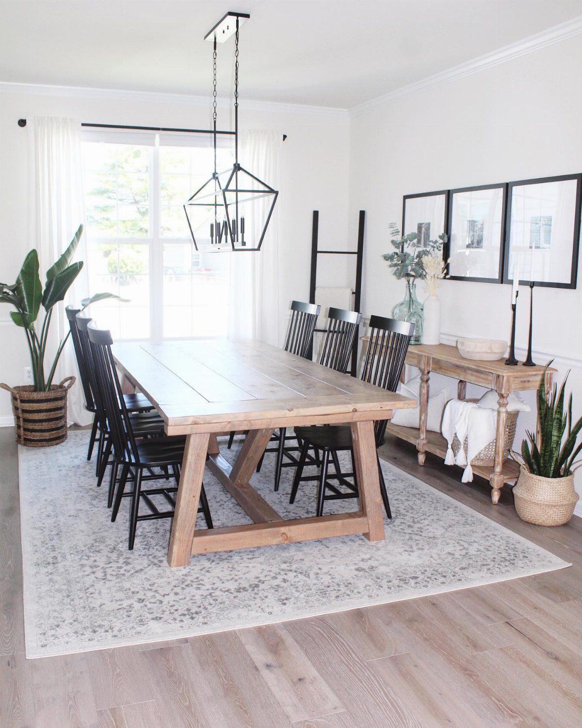 A large wooden farmhouse table with black chairs set in a bright, modern kitchen.