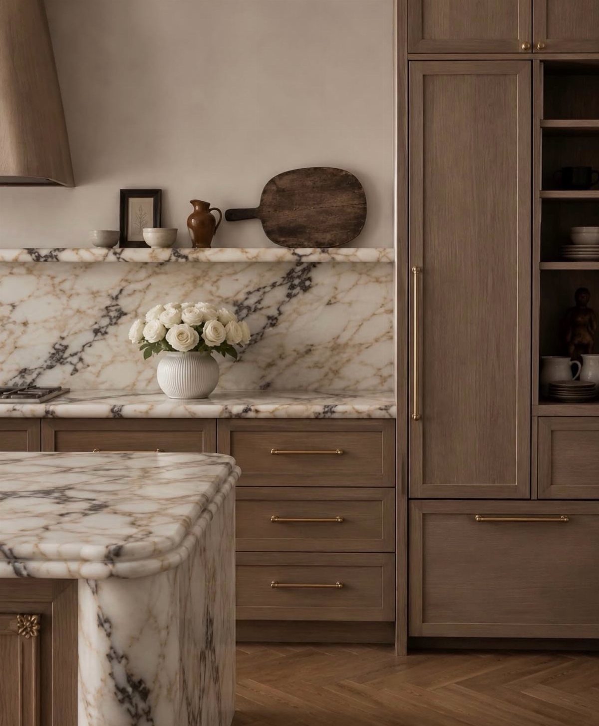Light wood kitchen cabinets with marble countertops and a wooden cutting board on the counter.