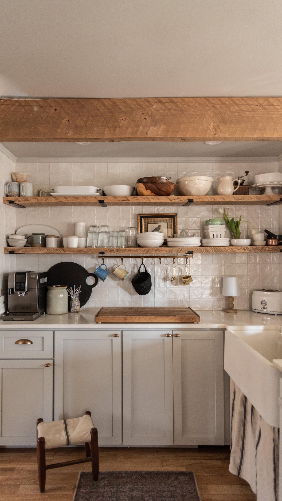 Wooden floating shelves holding white ceramic dishes and glassware against a tiled kitchen wall.