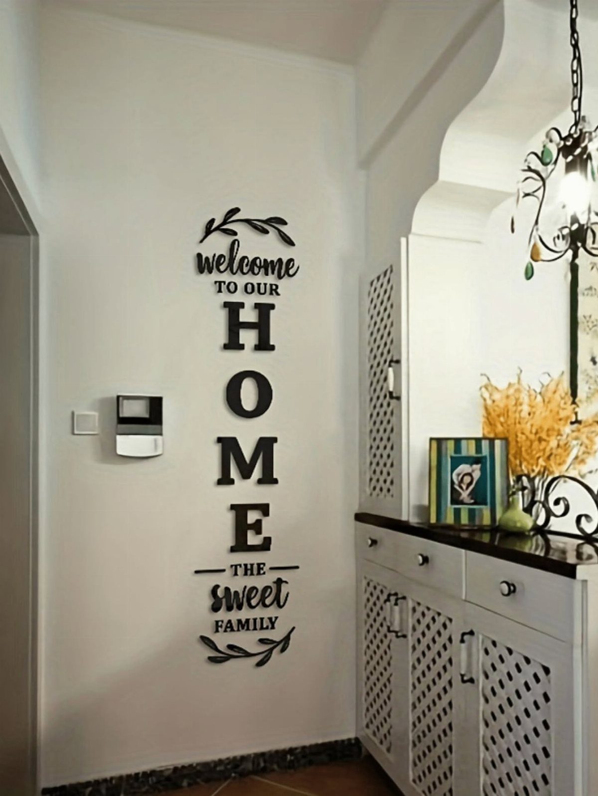 Black decorative wall sign with welcoming text mounted on a plain white wall.