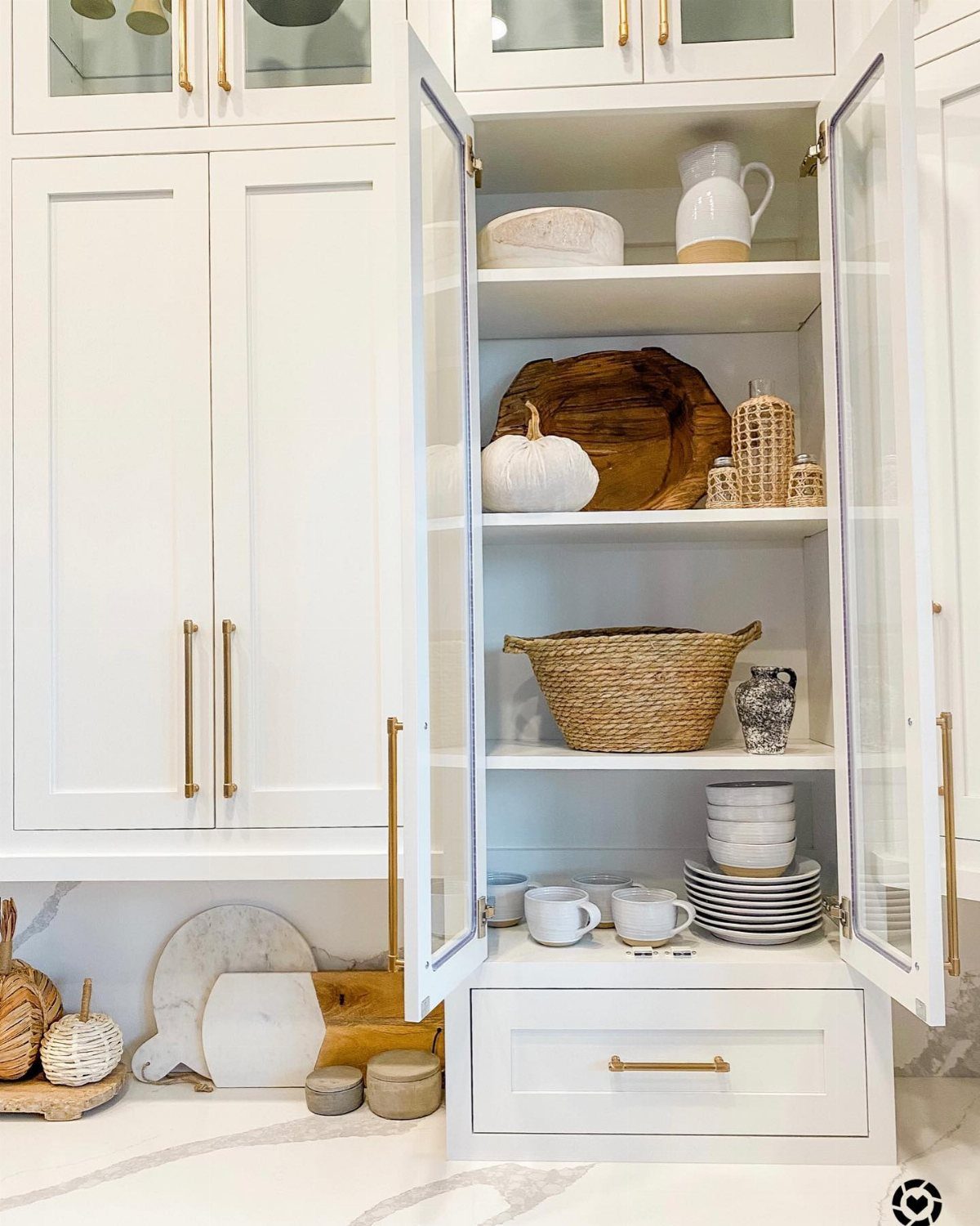 Open white kitchen cabinet displaying a white pumpkin, woven basket, and ceramic dishes on shelves.