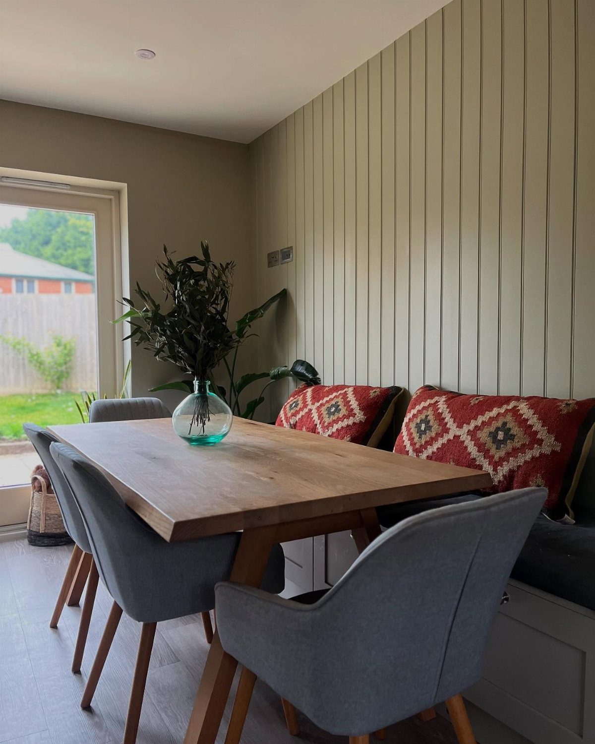 Wooden dining table with grey chairs and vertical wood paneling on the wall.