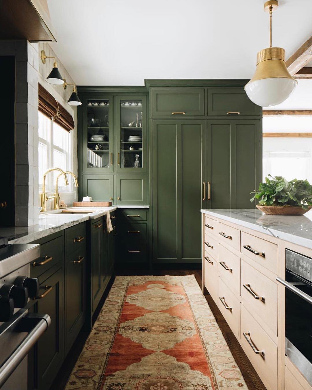 A patterned terracotta vintage rug on a dark wood floor in a green farmhouse kitchen.
