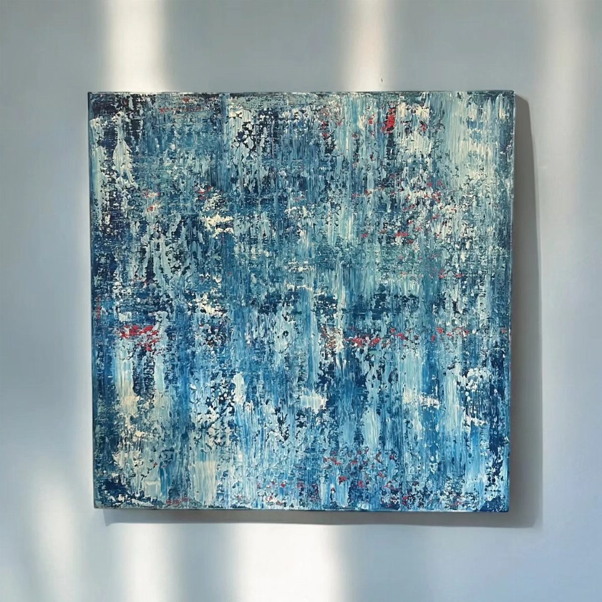 Abstract blue and white textured painting hanging on a light grey wall.