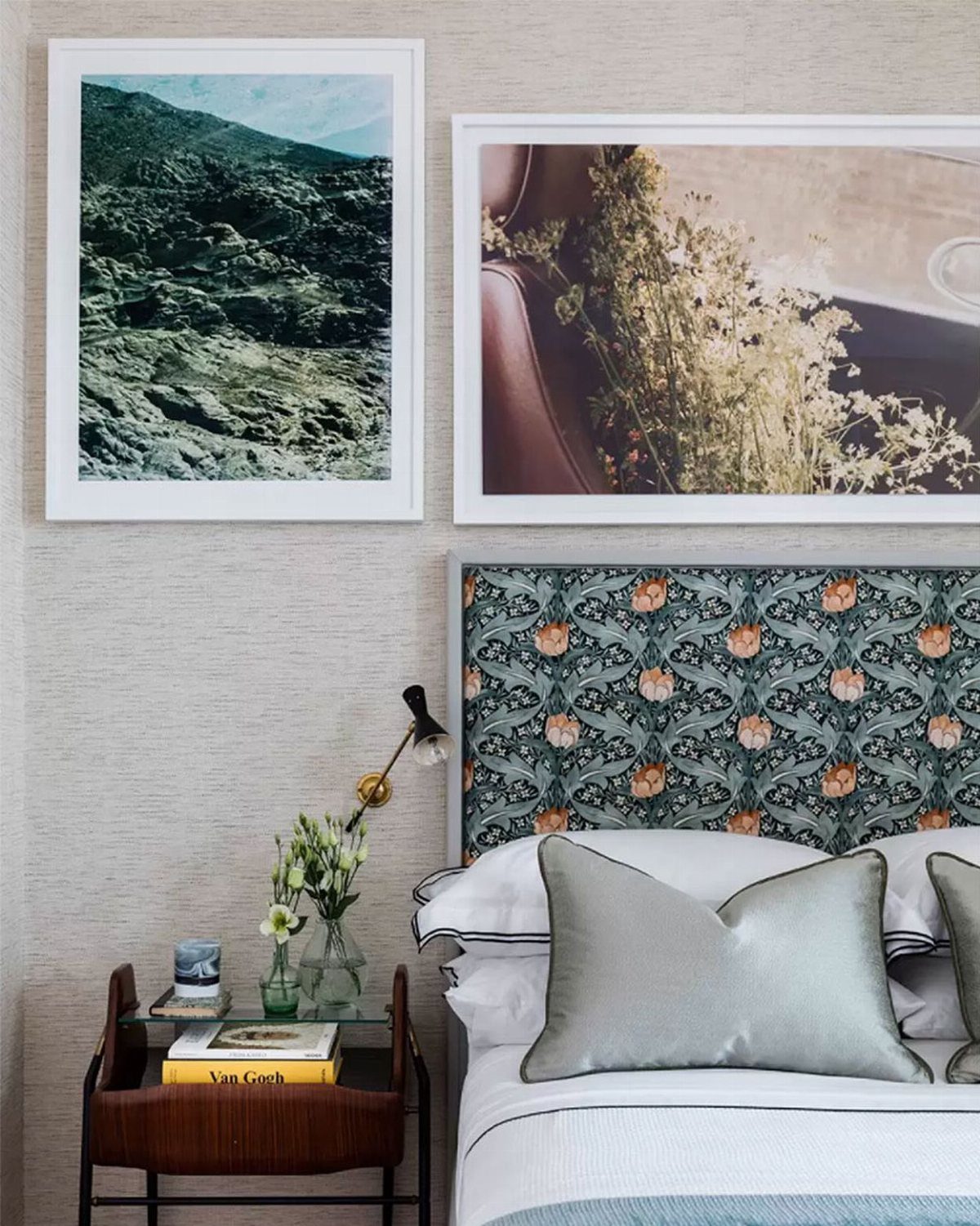 Patterned headboard with floral motifs next to a bed with silver pillows and framed art.
