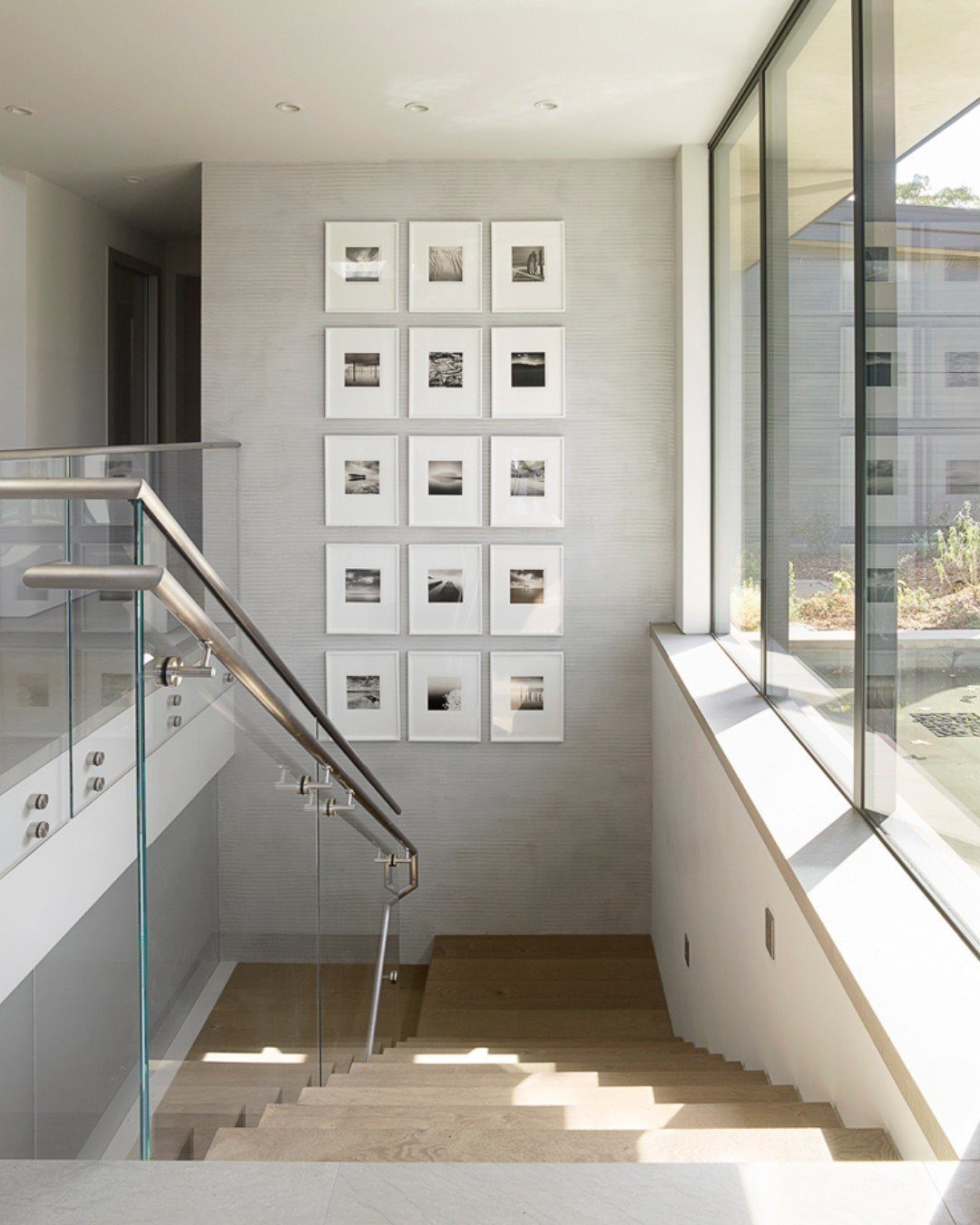 Modern staircase with glass railings and a large grid of framed black and white art.