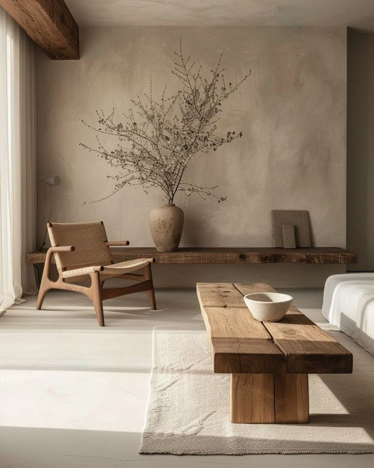 Dried branches in a ceramic vase sit on a wooden shelf in a minimalist room.