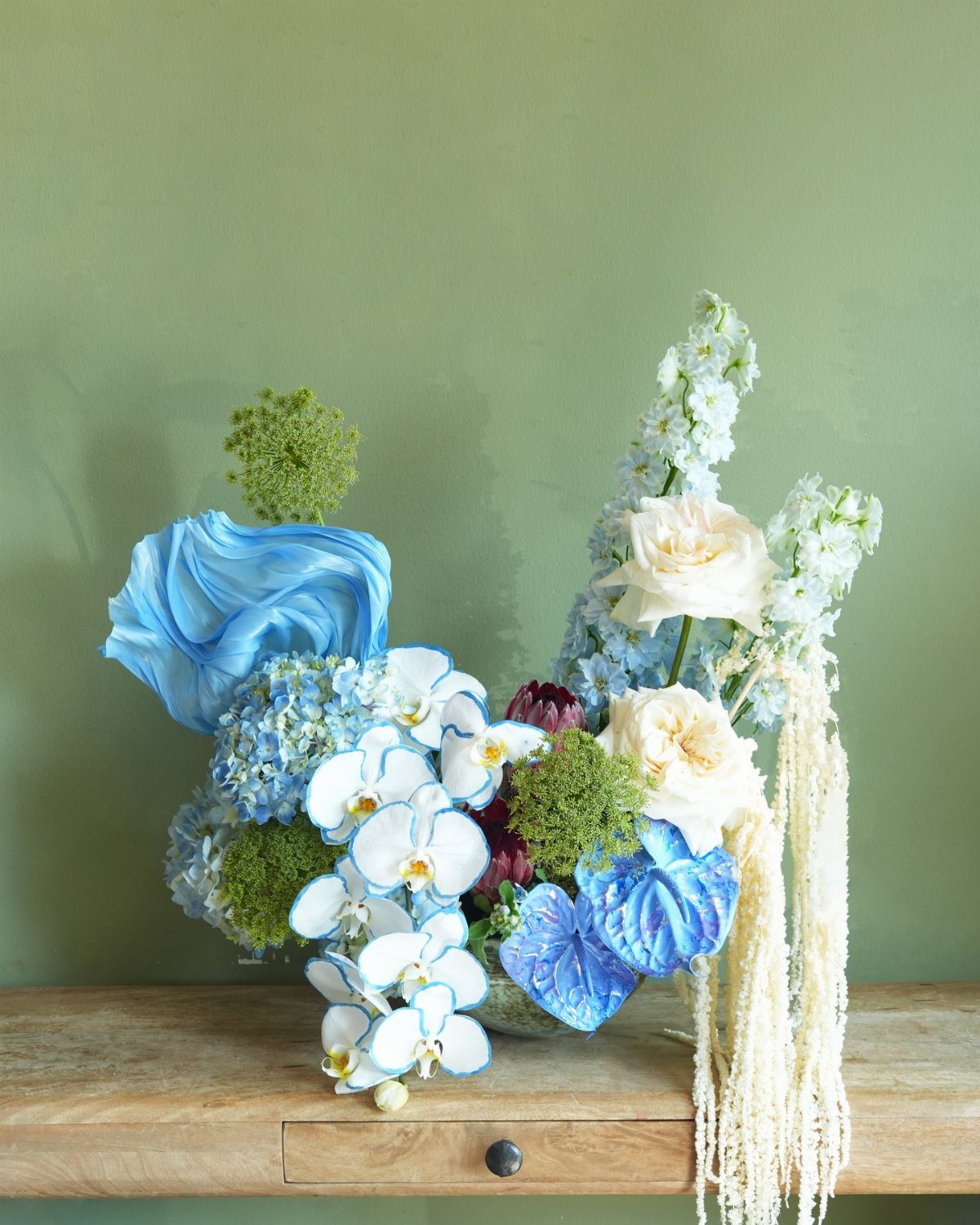 Blue and white floral arrangement with orchids and roses on a wooden table.