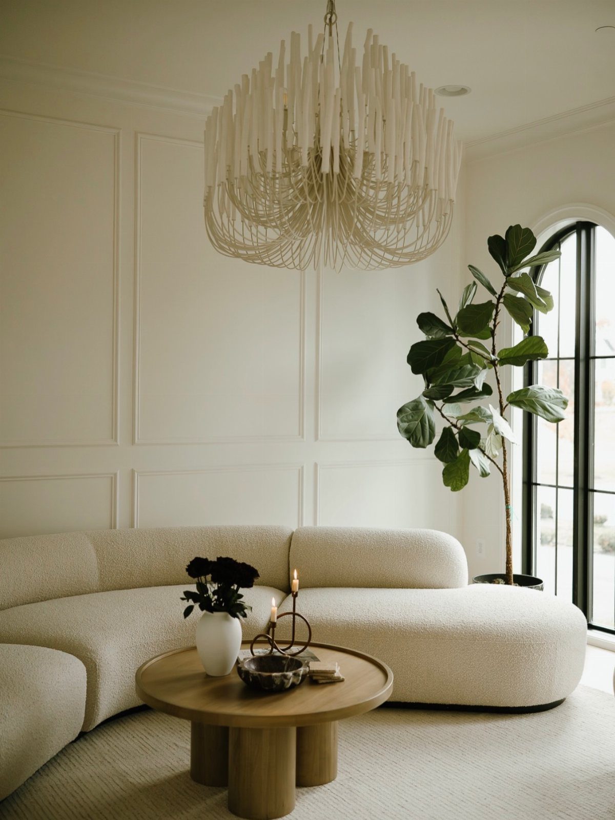 Curved cream sofa and round wooden coffee table in a bright, paneled room.