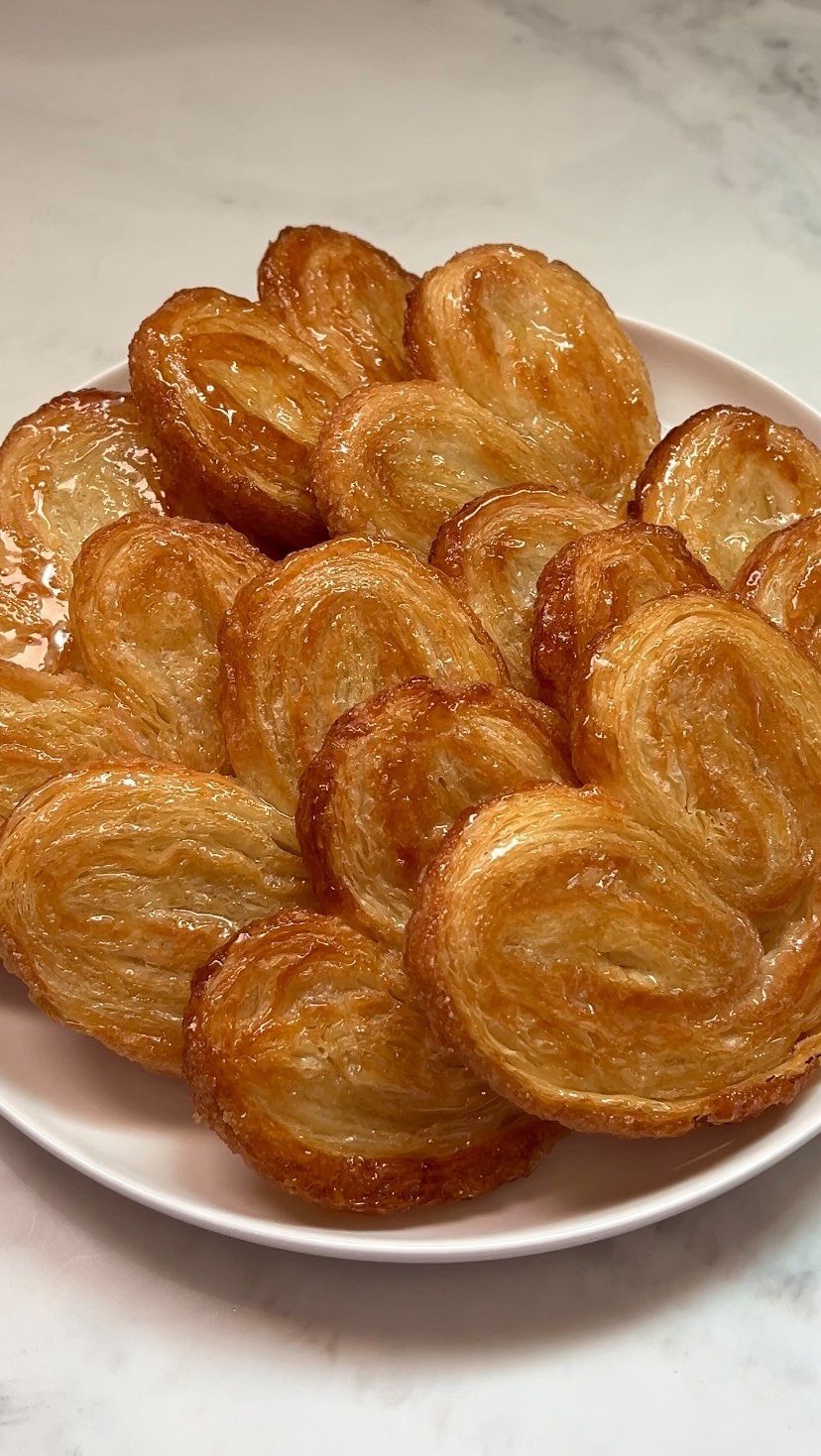 Golden glazed palmiers stacked on a white plate over a marble surface.