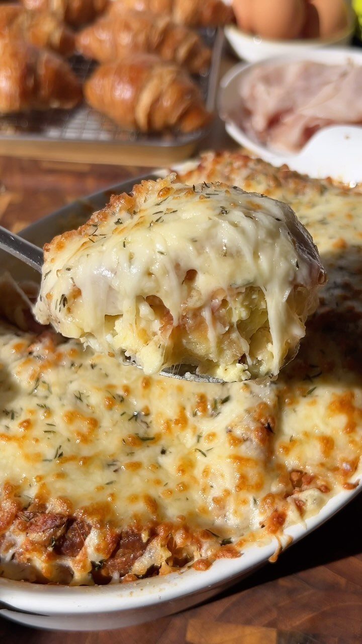 A metal spatula lifts a large, cheesy bite of breakfast casserole from a white dish.