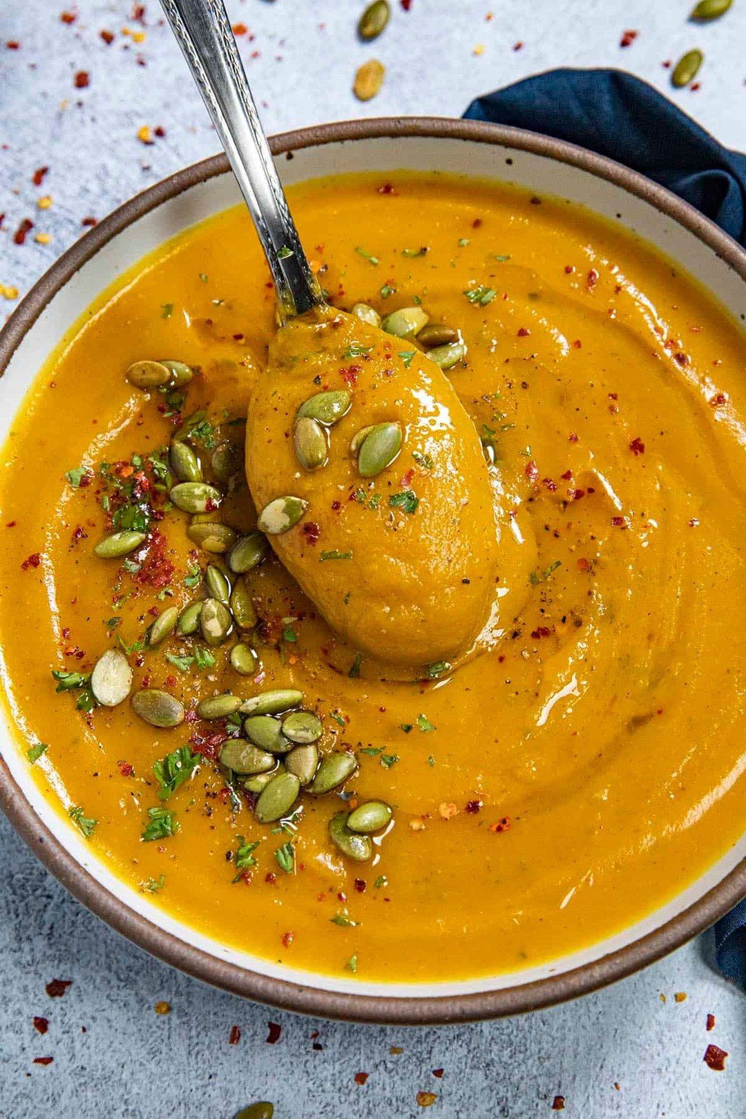 Orange butternut squash soup in a bowl topped with pumpkin seeds and chili flakes.