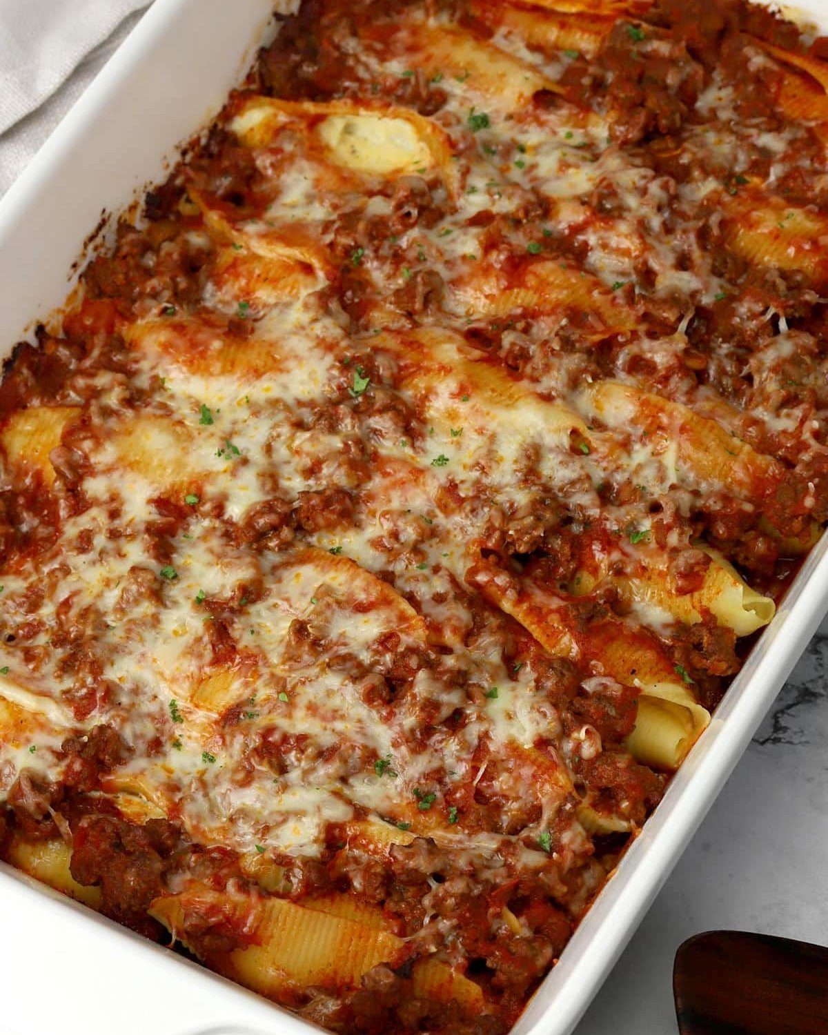 Baked stuffed pasta shells with meat sauce and melted cheese in a white dish.