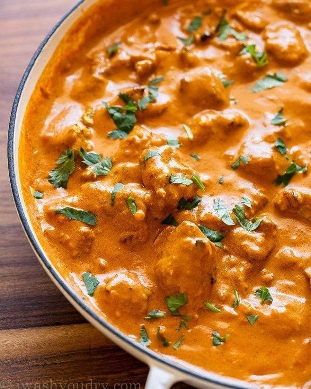 Creamy orange chicken tikka masala garnished with fresh green cilantro in a white bowl.