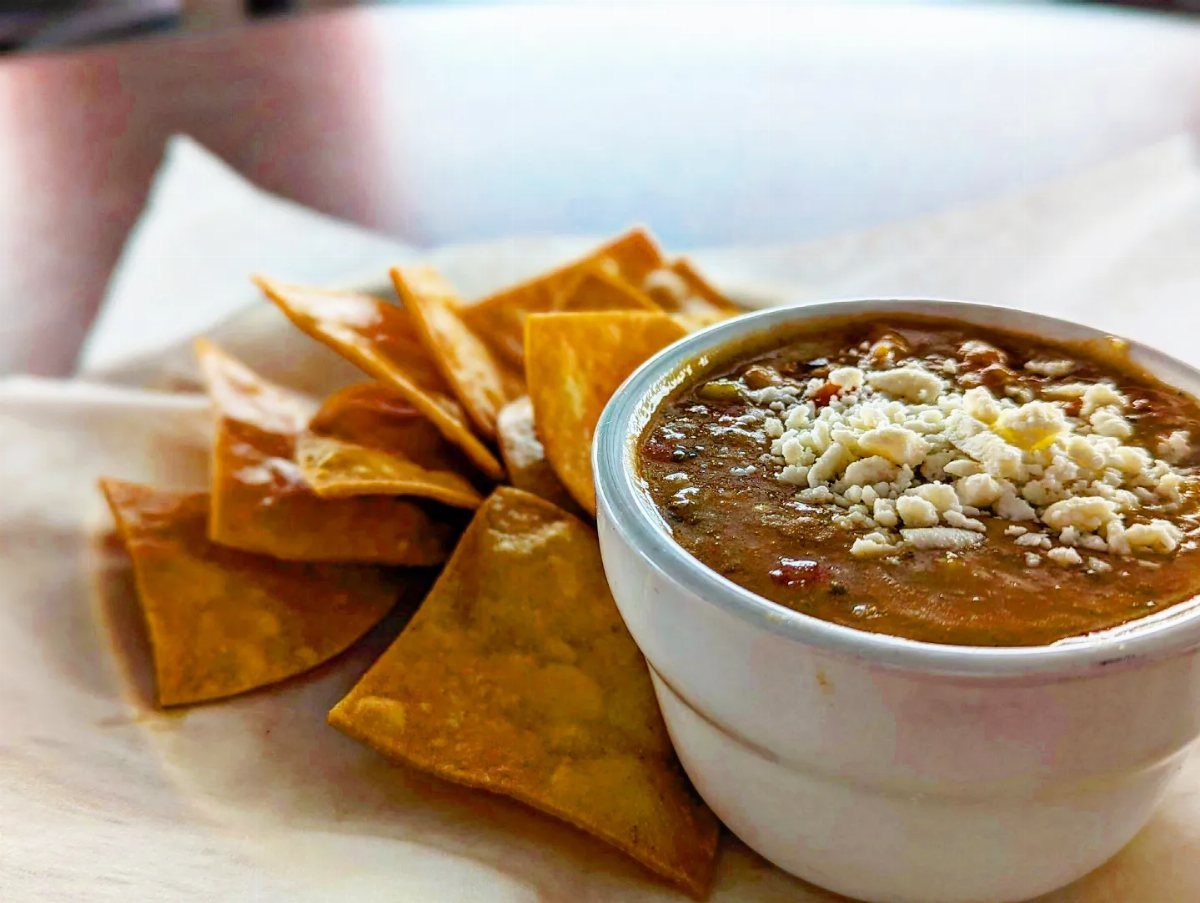 Chili topped with white cheese served in a white bowl with tortilla chips.