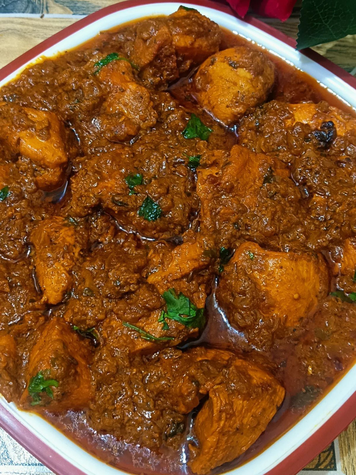 Chicken tikka masala with thick reddish-brown sauce and green herb garnishes in a white bowl.
