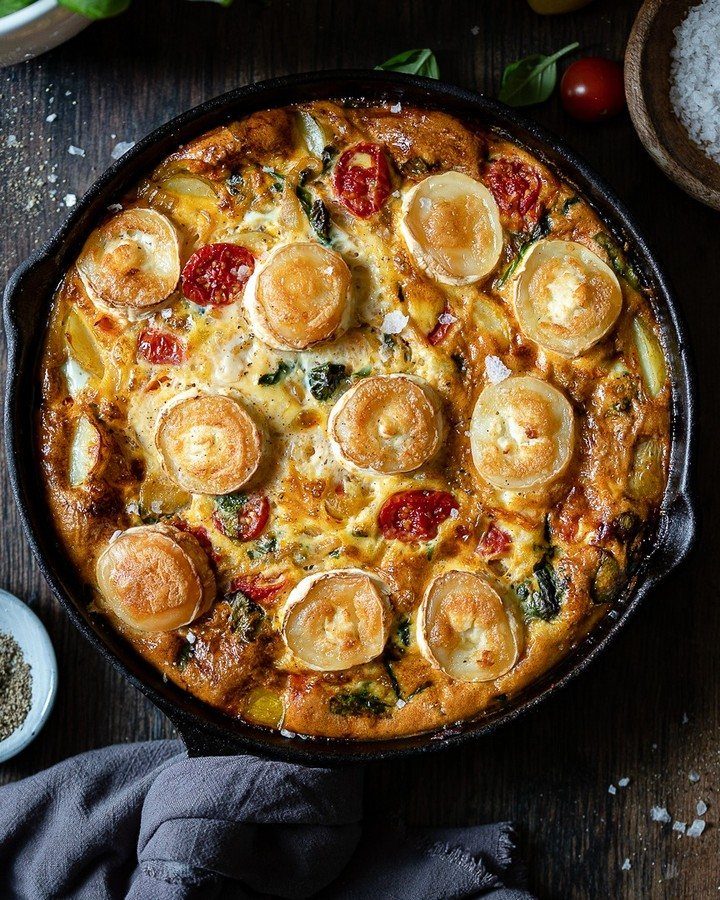 A golden frittata with goat cheese and tomatoes served in a black cast iron skillet.