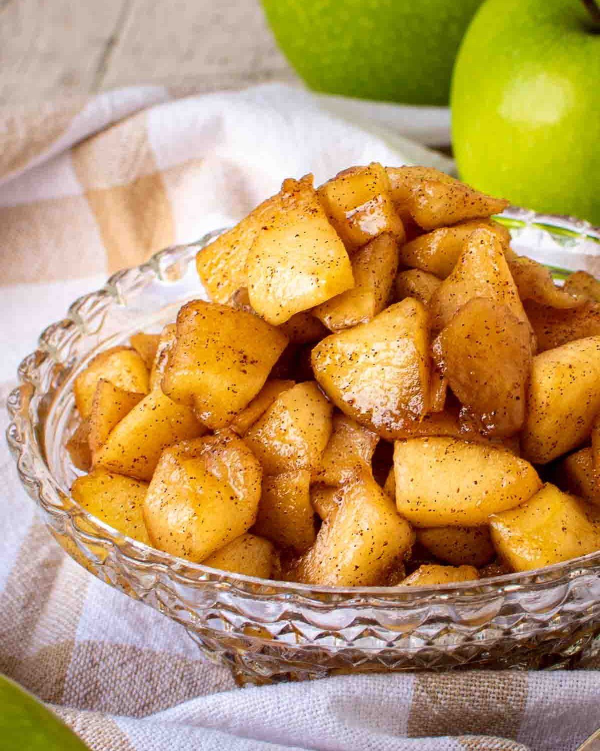 Spiced cooked apple chunks served in a clear glass bowl on a checkered cloth.
