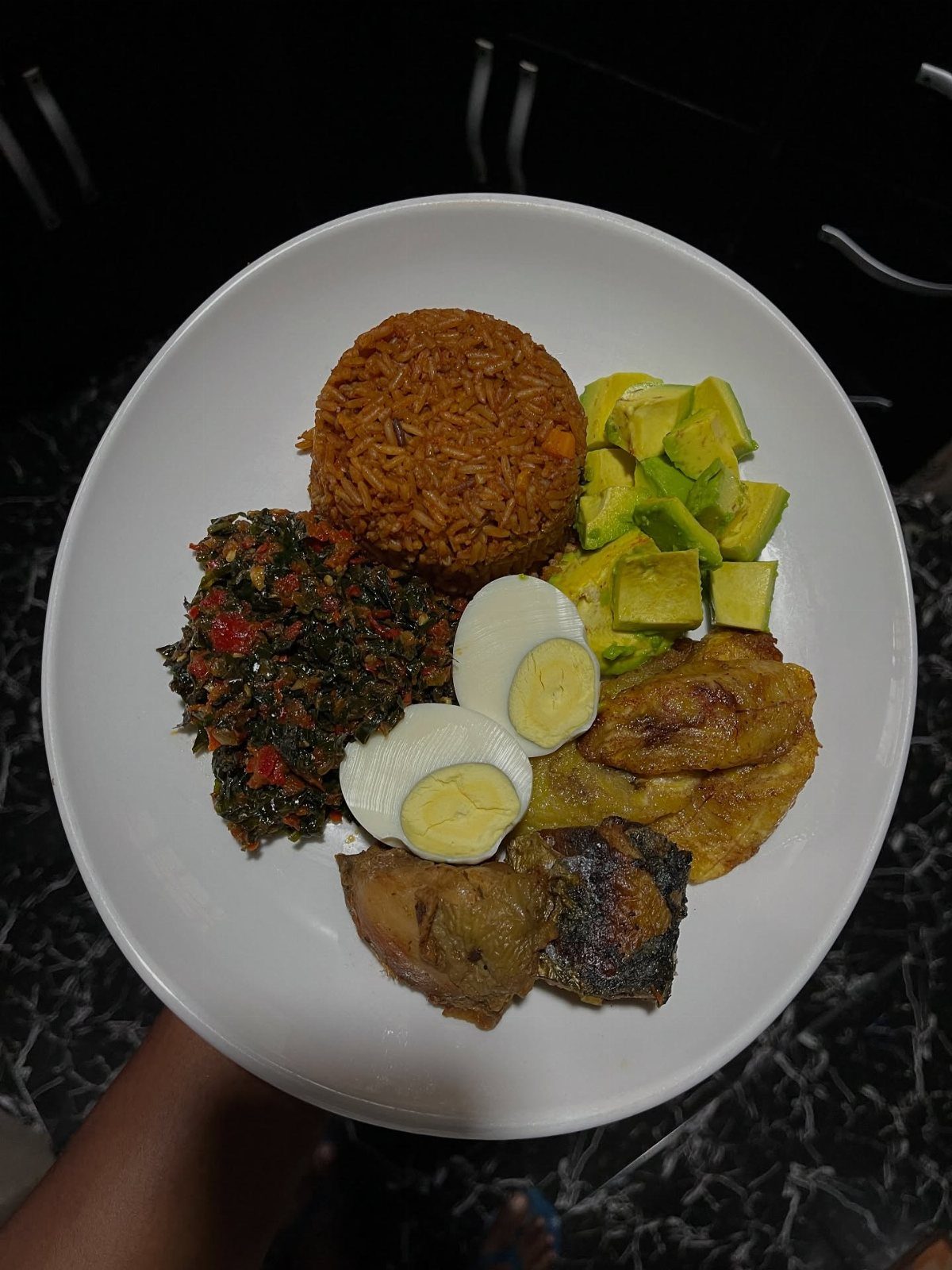 A white plate containing seasoned rice, avocado, hard-boiled eggs, plantains, and vegetables.